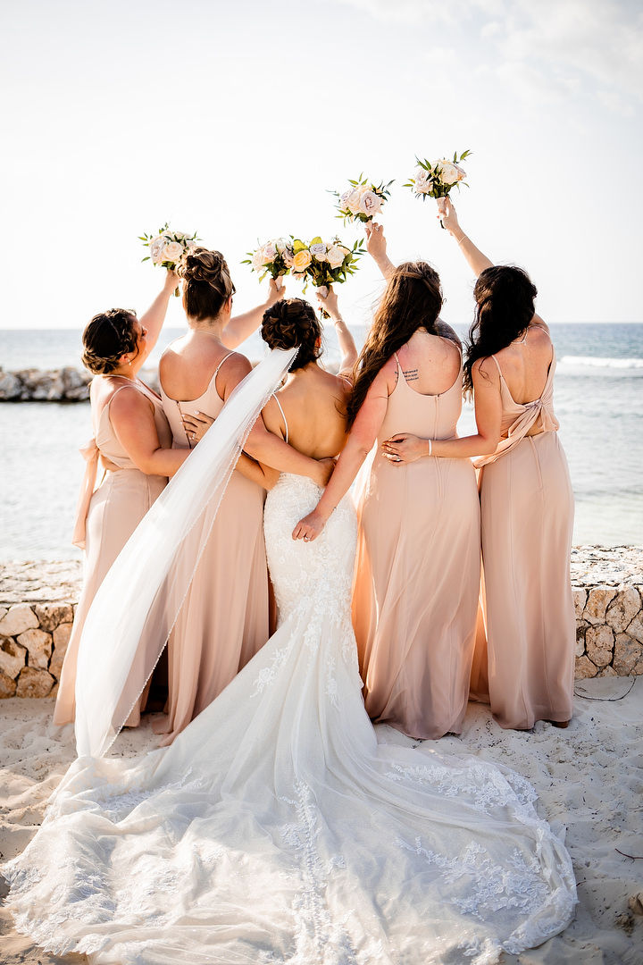 Bride and bridesmaids raising bouquets on the beach Ocho Rios Jamaica
